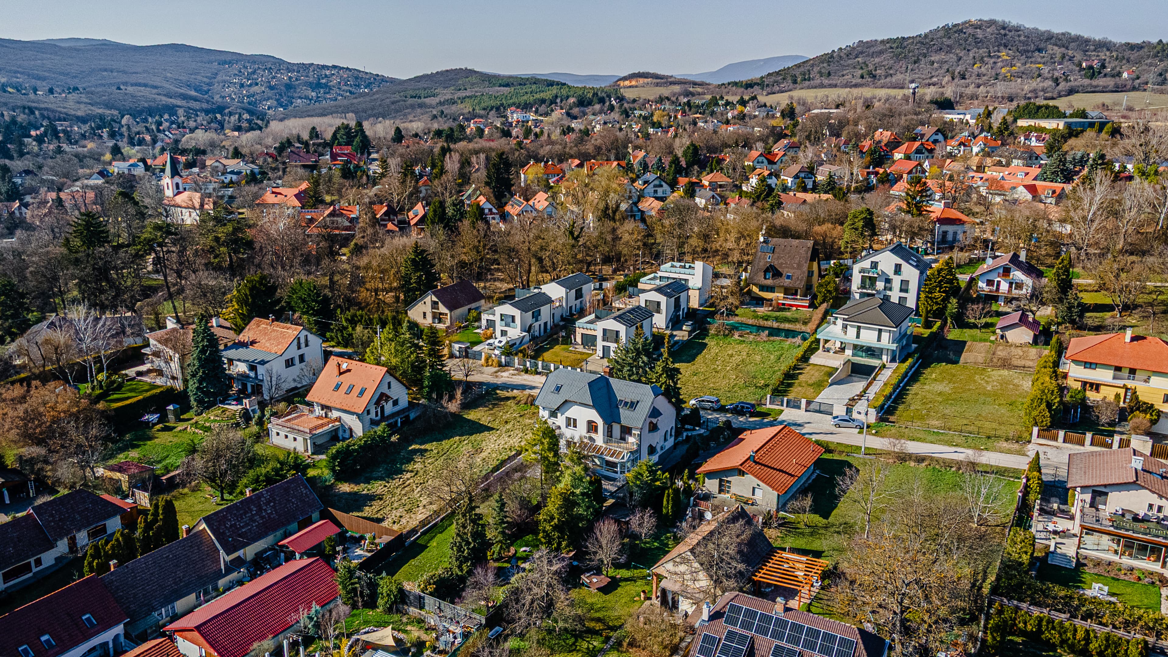 Aerial view of a village with red-roofed houses surrounded by forested hills and bare trees.