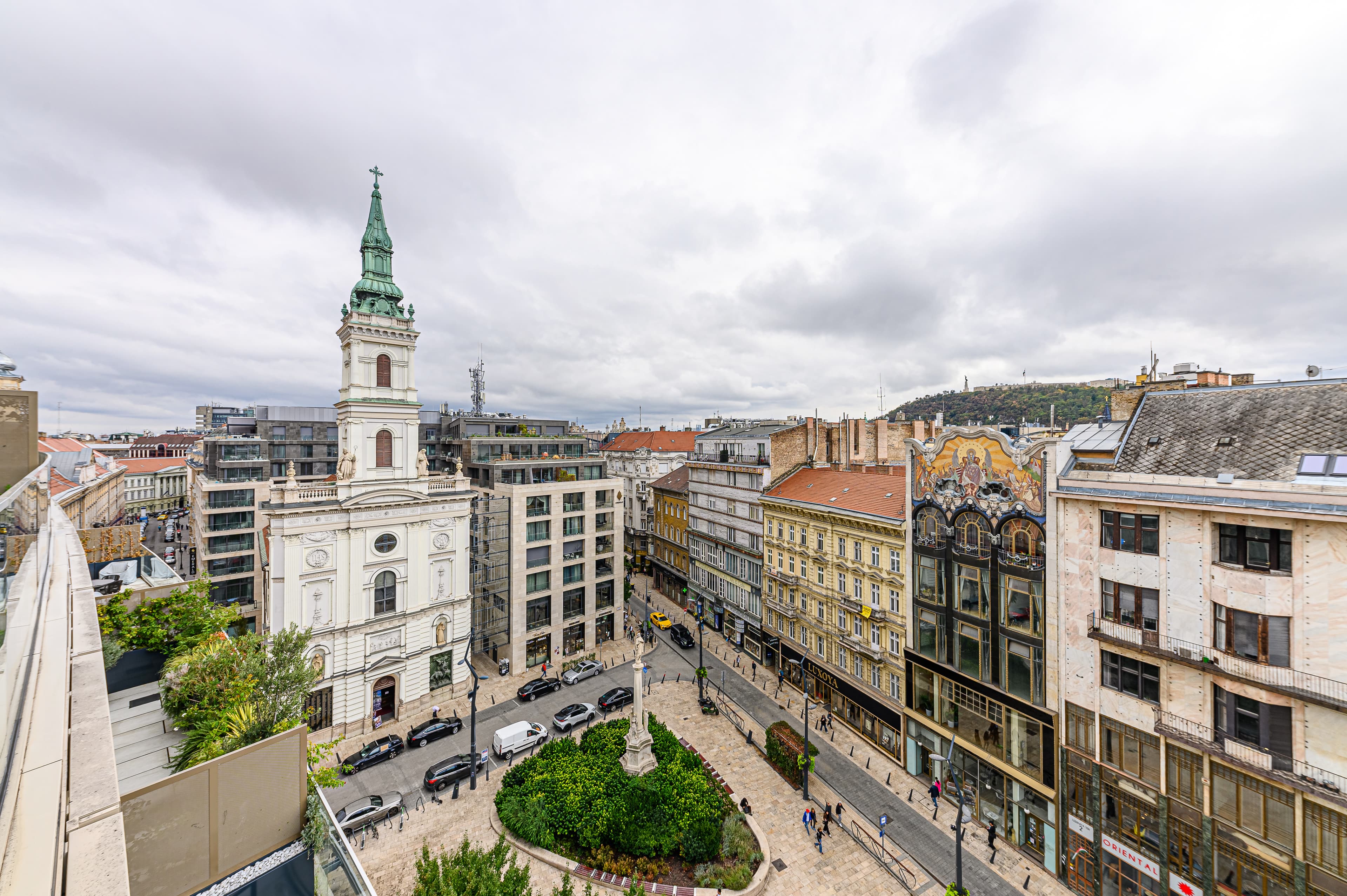 High-angle view of Budapest's historic buildings, including a white church and colorful mosaic facade.
