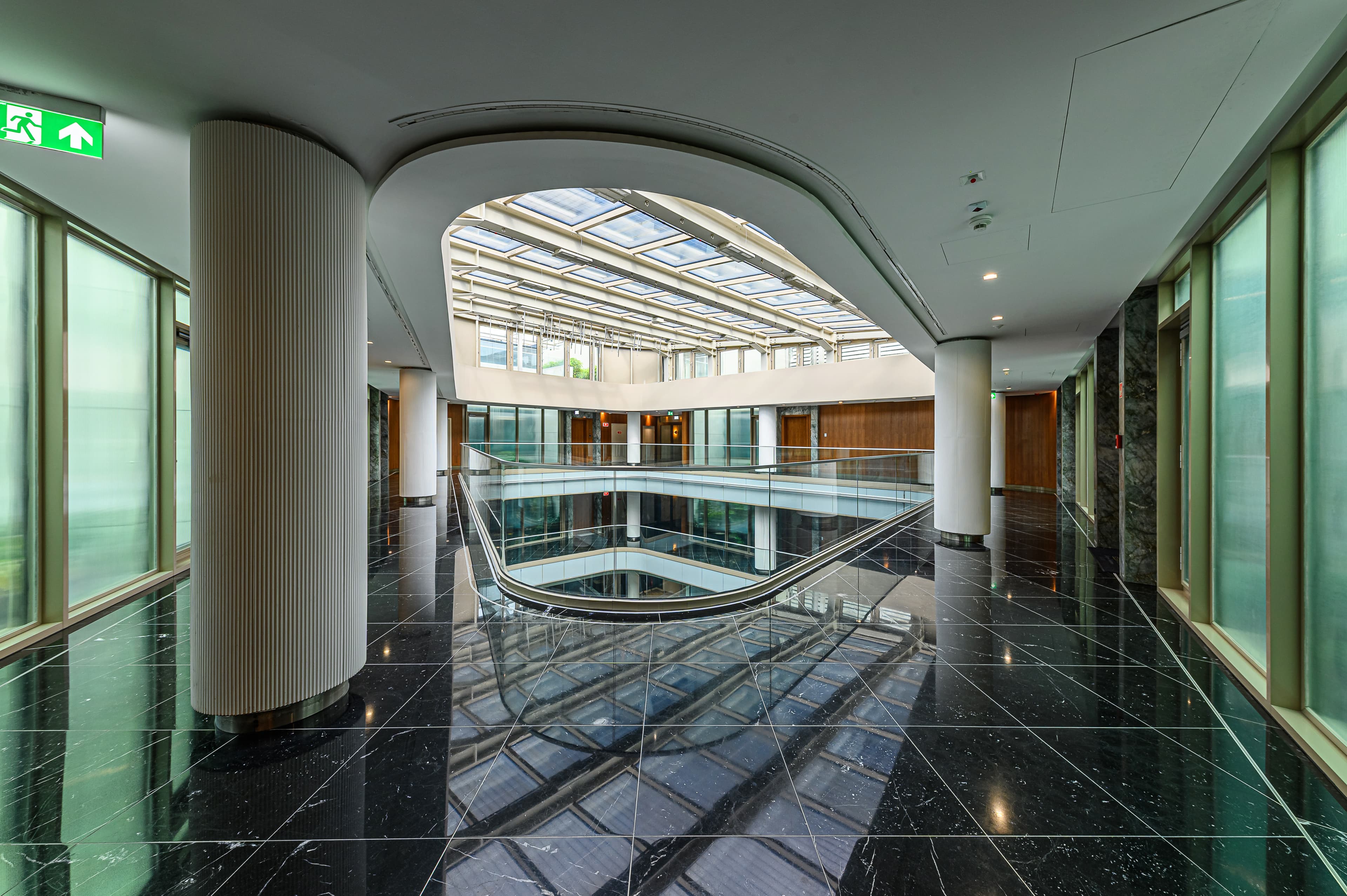 Modern atrium with polished black marble floors, white fluted columns, and a large central skylight.
