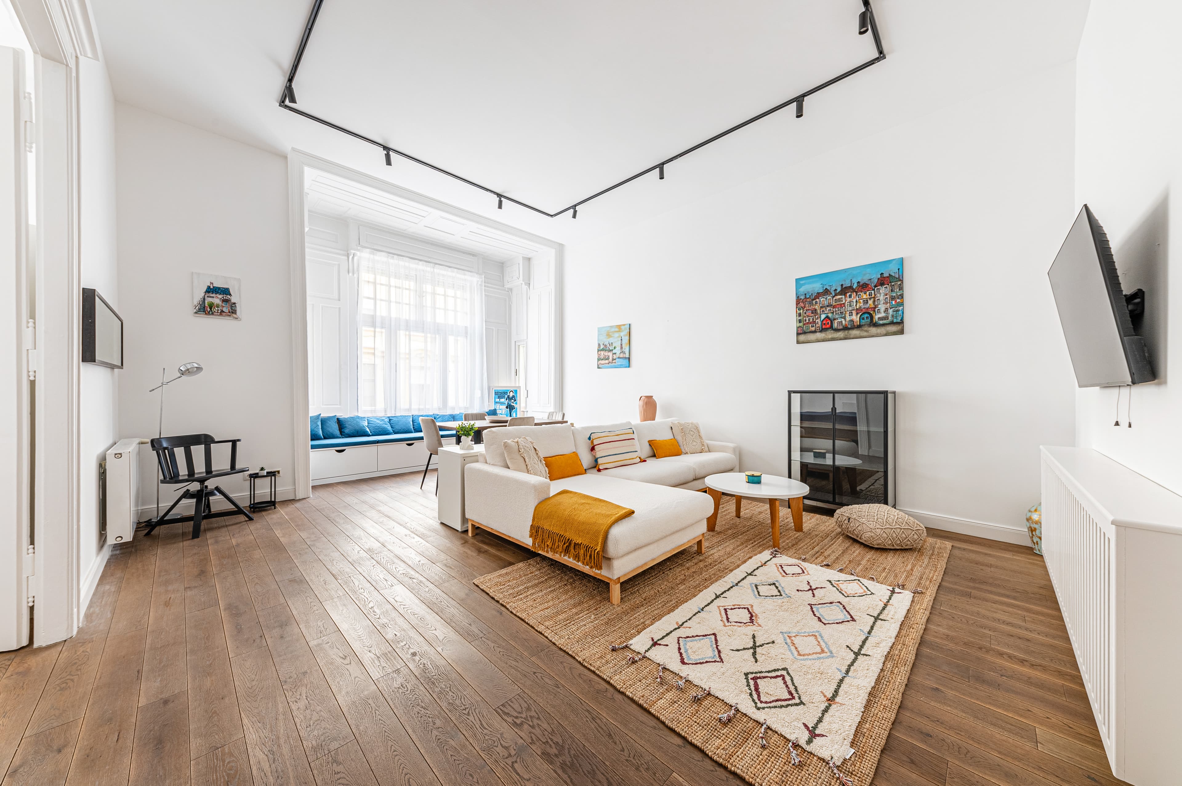 Bright modern living room with white sectional sofa, wooden floors, and large window bench.