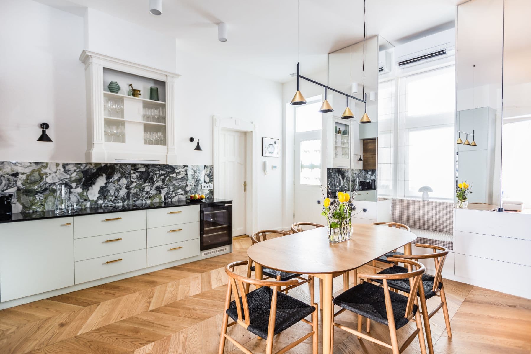 Modern kitchen and dining area with marble backsplash, wooden table, and herringbone wood floors.